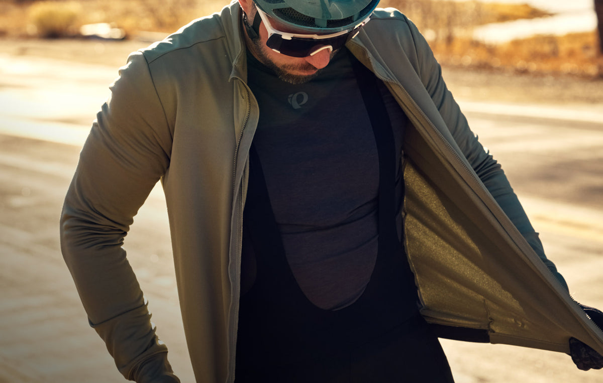 Close up image of male cyclist wearing a cycling base leayer and cycling bibs and zipping up his thermal jersey