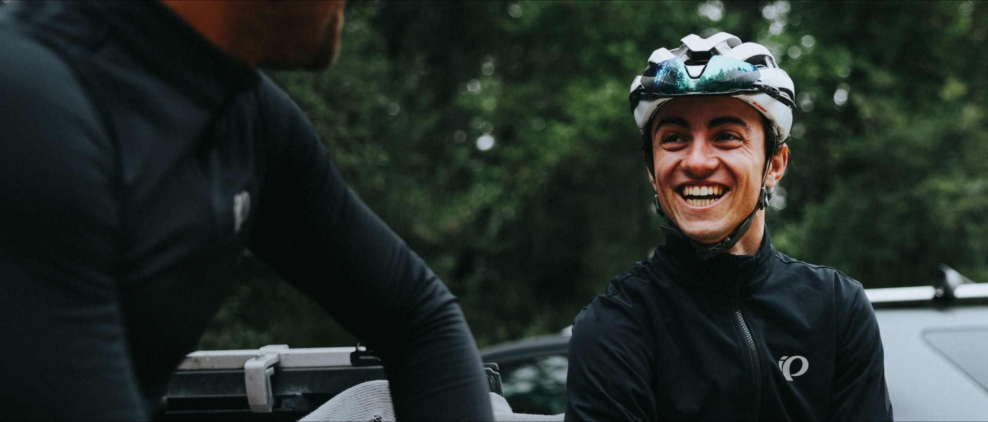 Person in cycling gear with helmet, standing outdoors with trees in the background
