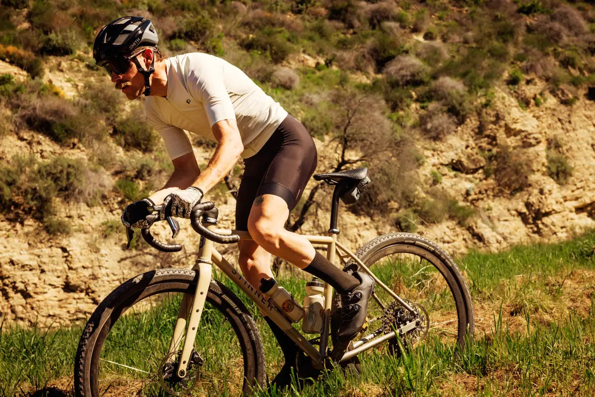 Person riding a bicycle on a grassy trail with a mountainous background