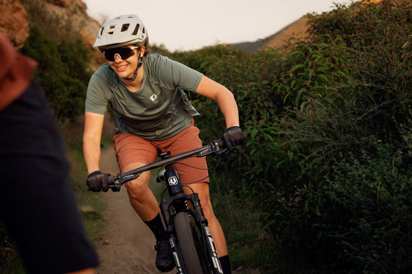 Female mountain biker riding down a dirt trail while wearing mountain bike shorts and a mountain bike jersey
