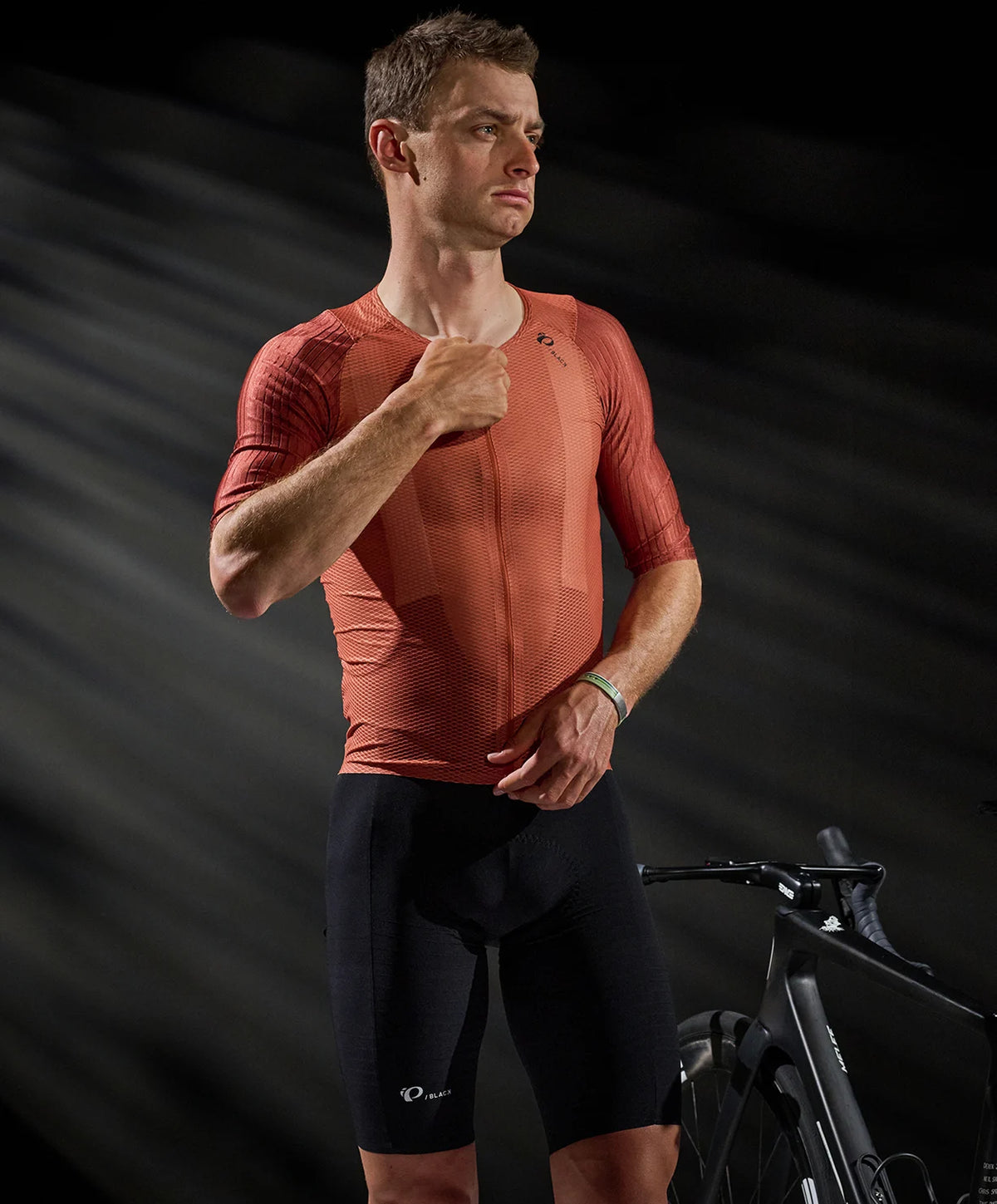 Man wearing a red cycling jersey and black shorts with a bicycle in the background
