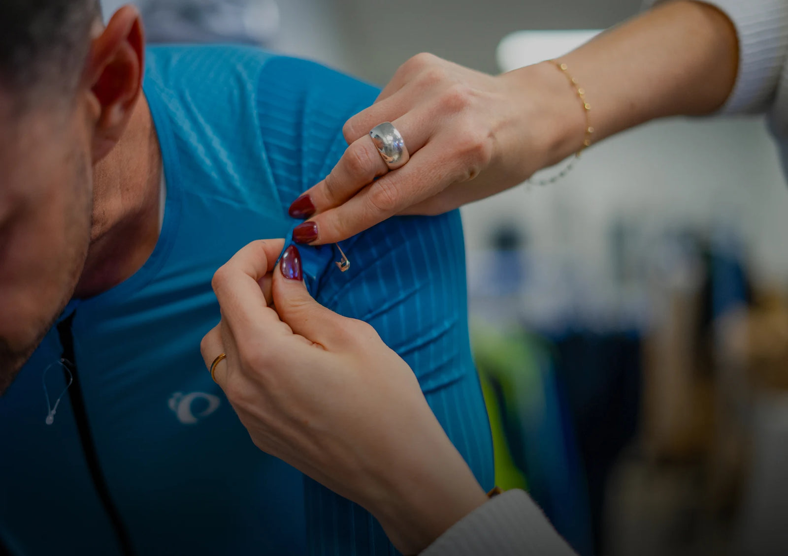 Person adjusting a small object on another person's blue shirt with a blurred background